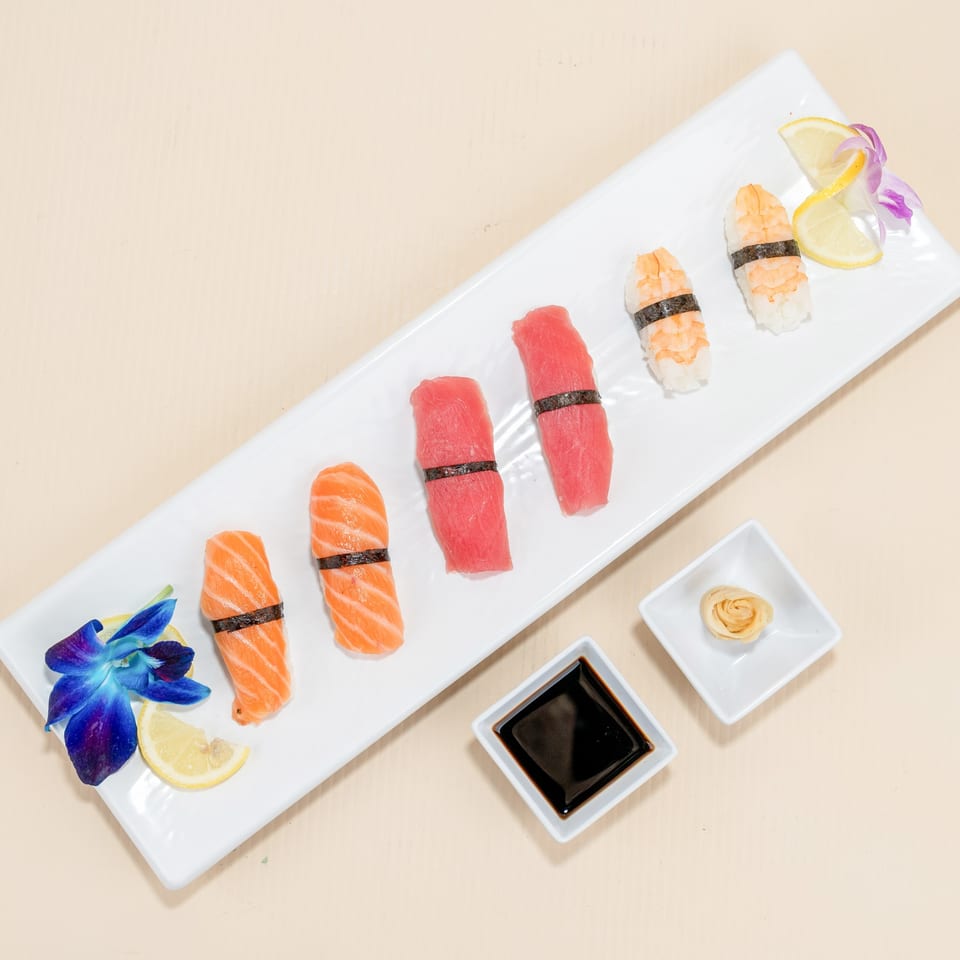 A white rectangular plate holds various sushi pieces, including salmon, tuna, and shrimp nigiri.