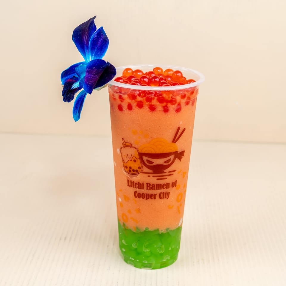 Litchi Ramen boba drink with orange and green layers, topped with red popping boba and a blue orchid.