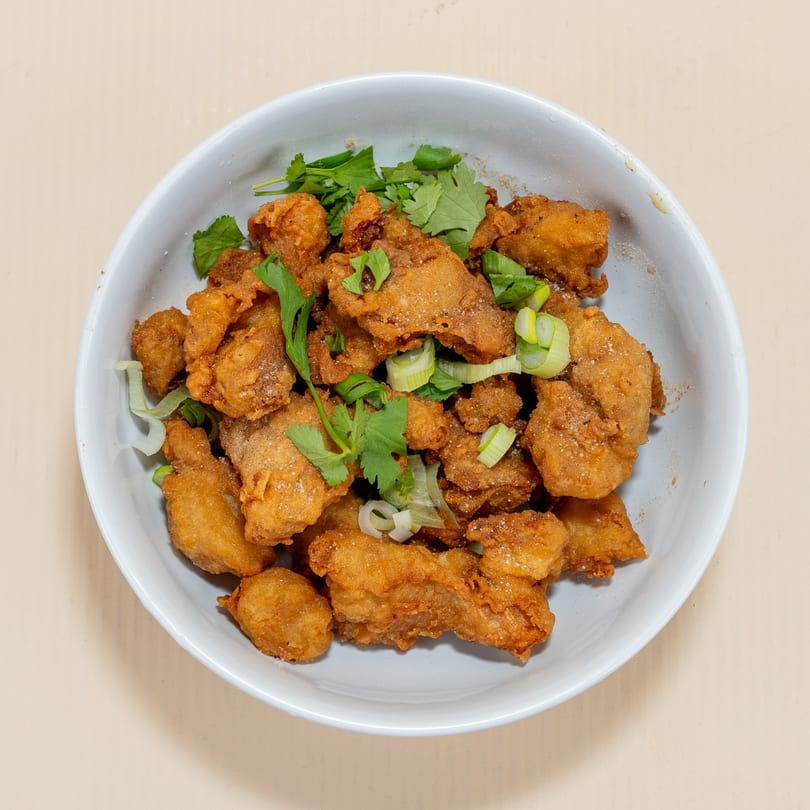 Crispy fried chicken pieces, seasoned and garnished with fresh cilantro and sliced green onions in a white bowl.