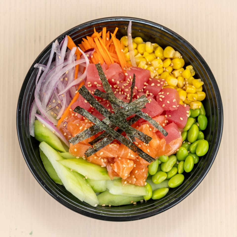 Colorful poke bowl with tuna, salmon, corn, edamame, cucumber, carrots, and red onions.