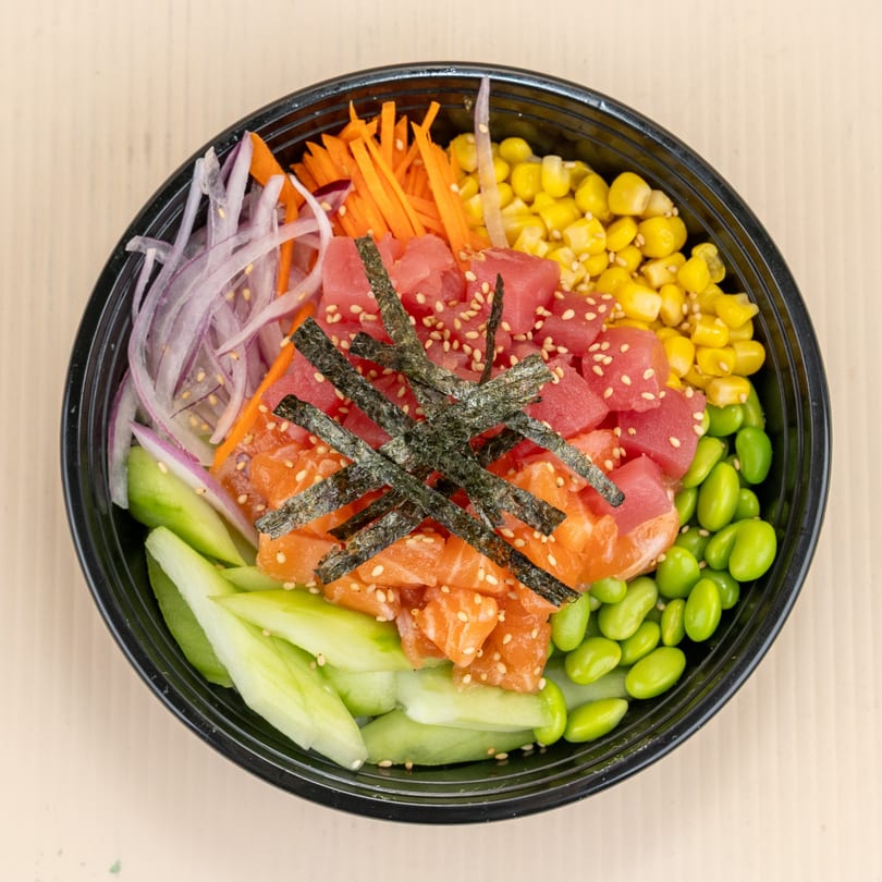 Colorful poke bowl with tuna, salmon, corn, edamame, cucumber, carrots, and red onions.